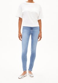 Vit kortärmad T-shirt som är kombinerad med ljusblå skinny jeans och silverfärgade ballerinaskor, med en enkel design och släta texturer.