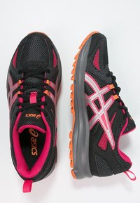 Baskets de sport noires avec une tige en maille. Présentent des accents roses et orange, une semelle rembourrée et un motif texturé sur le côté.