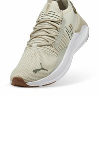 Beige Sportliche Schuhe mit einem strukturierten Strickobermaterial, weißer Mittelsohle, Gummisohle und grünen Akzenten. Puma-Logo auf der Seite sichtbar.