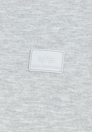 Hellgrau Sweatshirt aus weichem Stoff, mit einem strukturierten "Alpha Industries"-Label auf einem rechteckigen weißen Patch.