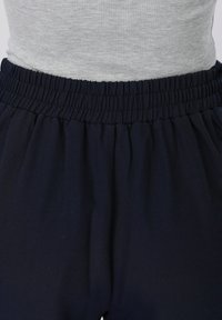 Λεπτομέρεια στη μέση με παντελόνι με ελαστική μέση σε ναυτικό μπλε χρώμα, συνδυασμένο με ανοιχτό γκρι ριπ μπλουζάκι που είναι βαλμένο μέσα.