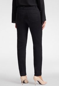 Mustat kapeat farkut, joissa on sileä pinta, kahdella takataskulla ja keskikorkealla vyötäröllä, yhdistettynä nude-korkokenkiin.