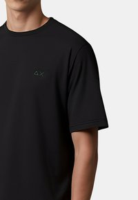 T-shirt nera a maniche corte realizzata in tessuto morbido, con un sottile logo ricamato in verde scuro sul petto, vestibilità rilassata e scollatura rotonda.