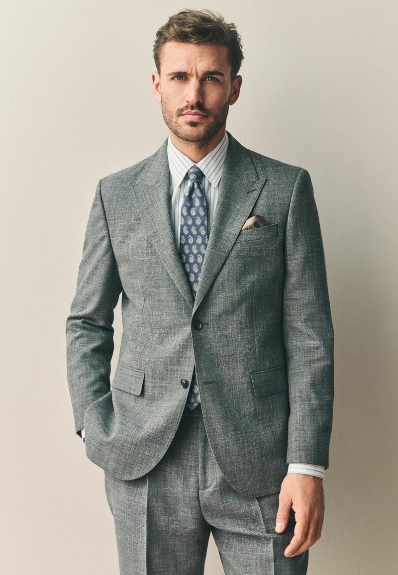 Hallitatud hall ülikond tekstureeritud kangast, millel on triibuline särk ja paisley stiilis lips. Tasku ruuduke lisab peene kontrasti. Korralikud õmblemise detailid.