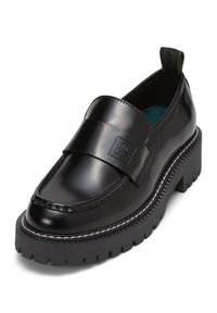 Mocassin en cuir noir avec une large lanière brillante, une semelle en caoutchouc épaisse et des coutures blanches. Présente un logo sur la lanière et une languette de traction à l'arrière.