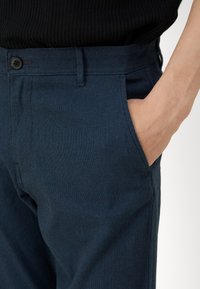 Námořnické modré kalhoty z rašlové tkaniny, s viditelnou kapsou, pasem se zapínáním na knoflík a upraveným střihem.