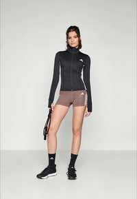 Svart zip-up jakke med hvite detaljer, brune treningsshorts, svarte sportssko og svarte ankelsokker. Enkelt og funksjonelt design.