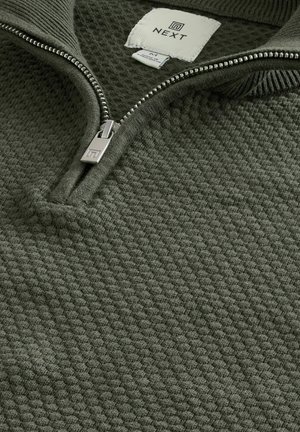Grüner Pullover mit Reißverschluss aus strukturiertem Strickstoff. Zeigt eine Nahaufnahme des Kragens, des silbernen Reißverschlusses und des Markenlabels.