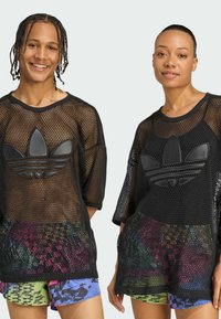 Black mesh oversized shirt with a textured black Adidas logo, featuring short sleeves and a colorful, patterned layer underneath.