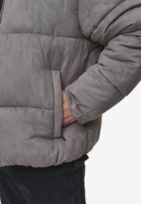 Pilkas pūkinis švarkas su minkštu, zomšos tipo audiniu, turi šoninę kišenę ir laisvą siluetą. Rankovės yra šiek tiek per didelės.