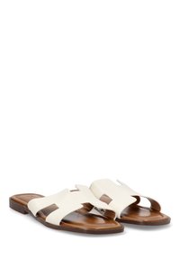 Sandalias de cuero blanco con un diseño recortado, suela plana marrón y acentos minimalistas para un aspecto limpio y moderno.