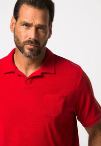 Rotes Polo-Shirt aus weichem Stoff, mit einem Kragen und einer Brusttasche. Kurze Ärmel und ein einfarbiges Design mit einer strukturierten Optik.