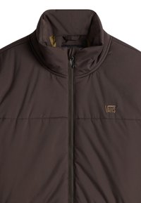 Chaqueta marrón acolchada con cuello alto, cremallera frontal y logo marrón de Vans en el pecho. El material parece suave e insulated.