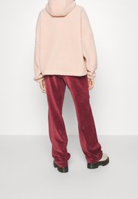 Ljusrosa fluffig hoodie med huva, i kombination med djupröda kordflorsbyxor. Byxorna har vertikal ribbning; skorna har en kraftig svart sula.