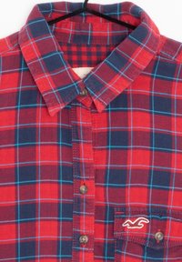 Camicia a bottone a quadri rossi e blu con colletto, caratterizzata da dettagli blu, una tasca sul petto e ricamo del marchio sulla tasca.