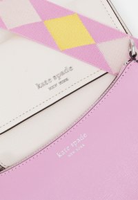 Portafoglio in pelle rosa con dettagli in argento, dotato di interno bianco. L'esterno presenta una tracolla con motivo rosa e giallo.