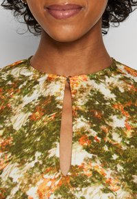 Robe à motifs floraux avec une palette de couleurs verte, orange et blanche. Présente un col rond avec un détail en forme de clé à l'avant.