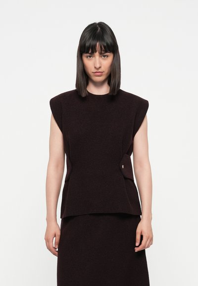 Burgunderfarbene ärmellose Bluse mit strukturierten Schultern, seitlichen Taschen und einem glatten, strukturierten Stoff. Kombiniert mit einer passenden Unterteilung.