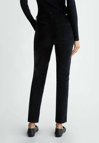 Pantaloni neri slim-fit con una trama liscia e vita media. Presentano due tasche posteriori e dettagli di branding discreti.