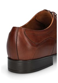 Brązowy skórzany but o gładkiej teksturze, zaokrąglonym kształcie i czarnej gumowej podeszwie. Posiada szczegółowe przeszycia wzdłuż cholewki.