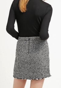 Jupe à motif pied-de-poule noir et blanc, avec une fermeture éclair au dos et un ourlet effiloché. Fabriquée en tissu texturé.