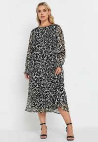 Svart och vit mönstrad midiklänning med långa genomskinliga ärmar, rund halsringning, elastisk midja och sidan slit. Slät, flödig textur.