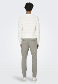 White striped sweater with a round neckline, paired with light gray tailored pants. The outfit is completed with white athletic shoes.
