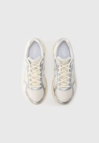 Białe i szare buty sportowe z siateczkową cholewką, odblaskowymi elementami, beżową podeszwą i sznurowanym fasonem. Logo ASICS na języku.