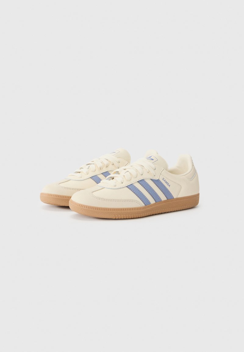 Cremefarbene Sneakers mit blauen Streifen, strukturiertem Gummiboden, runder Zehenform und Schnürdesign. Mit Logodetail an der Seite.