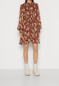 Blommönstrad klänning med långa ärmar, åtstramad midja och rund halsringning. Färgerna inkluderar brunt, rosa och kräm. Bärs med vita klackstövlar.