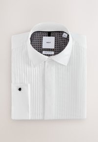 Valkoinen, 100 % puuvillainen paitapusero, jossa on frillat edessä, ryhdikäs kaulus ja kontrastivärinen kuvioitu sisävuori. Yksittäinen kalvosin, jossa musta nappi.