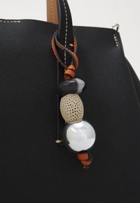 Borsa nera in tessuto con un ciondolo di perline nere e argentate e un accento in pelle arancione. Il design è elegante e moderno.