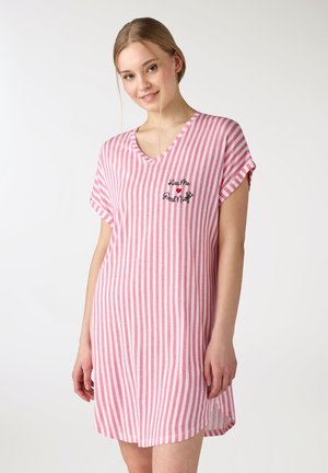 Młoda kobieta w różowo-białej sukience w pionowe paski z napisem „Kiss Me Good Night” i wzorem serca na piersi.