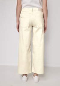 Pantalons large en denim jaune clair, avec des poches arrière et une taille haute. Présente une ceinture simple et un minimalisme dans les détails.