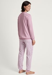 Maglietta lunga rosa chiaro a maniche lunghe con colletto rotondo abbinata a pantaloni rosa chiaro con motivo a piccoli fiori e polsini a costine.