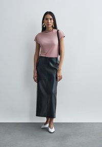 Jasnoróżowa dopasowana bluzka z krótkim rękawem w połączeniu z czarną skórzaną spódnicą midi. Białe szpilki z zaostrzonym noskiem i duże okrągłe kolczyki.