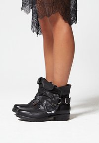 Bottes courtes en cuir noir avec un design à revers, dotées de lacets, de ferrures décoratives et d'une finition texturée. Semelle plate pour plus de stabilité.