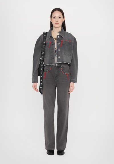 Cropped gray denim jacket with red stitching and pockets, paired with gray trousers featuring red accents. Model holds a black strap bag.