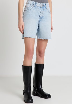 Shorts di jeans azzurri a vita alta con orli sfrangiati, indossati con stivali neri in pelle al ginocchio e una maglia grigia infilata dentro.