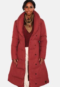 Lang rød dunjakke med stor krage, med svarte knapper og sidelommer. Brukt over en burgunder genser og et mønstret skjerf.