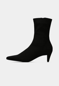 Μαύρο μποτάκι αστραγάλου από μαλακό ύφασμα με μυτερή μύτη και λεπτό τακούνι. Σχεδίαση χωρίς ραφές και ορατά μεταλλικά μέρη.