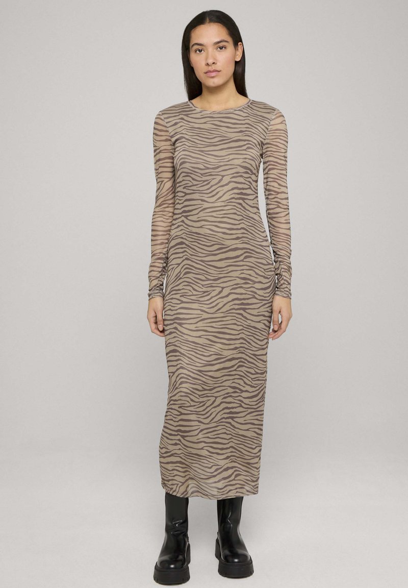 Dolga obleka z dolgimi rokavi z vzorcem zebrinega črtja, izdelana iz prosojne tkanine. Ima okrogel izrez in je kombinirana s črnimi gležnjarji.