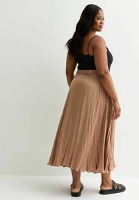 Langer beiger plissierter Rock mit weicher Textur; kombiniert mit einem schwarzen, figurbetonten Tanktop und schwarzen Slip-On-Sandalen. Zeigt die Rückansicht und die Details des Bunds.