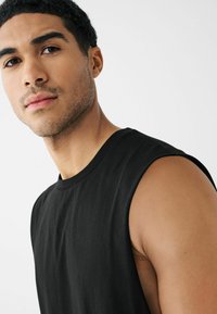 T-shirt noir sans manches en coton, avec un col rond et une coupe droite, présenté sur un fond clair.