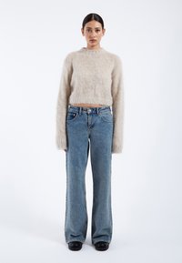 Light beige fluffy sweater with a high neckline, paired with blue wide-leg jeans and black platform shoes, set against a white background.