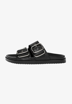 Schwarze Lederschlittensandalen verfügen über zwei große silberne Schnallen, eine flache Sohle und eine strukturierte Laufsohle. Das Design ist minimalistisch und modern.