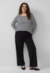 Gestreept shirt met lange mouwen in marineblauw en wit katoen, een ontspannen pasvorm, gecombineerd met zwarte broek met wijde pijpen en zwarte slingback schoenen.