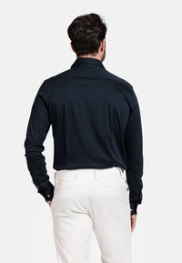 Marineblauwe overhemd met lange mouwen, een gladde textuur, knoopmanchetten en een spitse kraag, gecombineerd met crèmekleurige broeken.