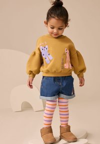 Żółta bluza z wesołymi wzorami zwierząt, dżinsowe szorty, paskowane rajstopy w różowym i pomarańczowym kolorze oraz brązowe botki za kostkę. Miękkie tekstury i jaskrawe kolory.