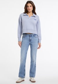 Felpa azzurra cropped con colletto, abbinata a jeans azzurri a vita alta e sneakers beige con lacci marroni.
